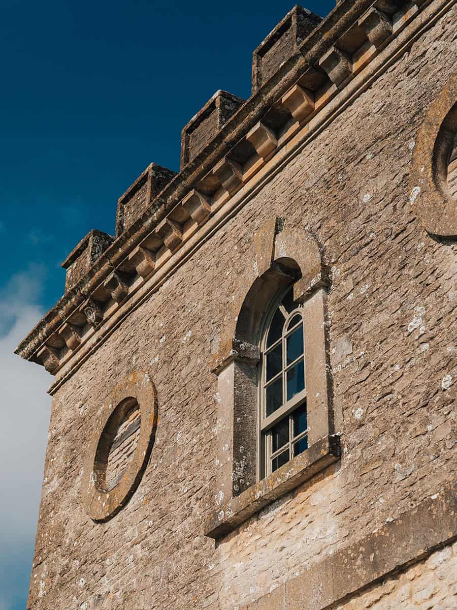 Ivy Lodge castellated tower detail with battlements, oculus windows, and arched stonework, Cotswolds